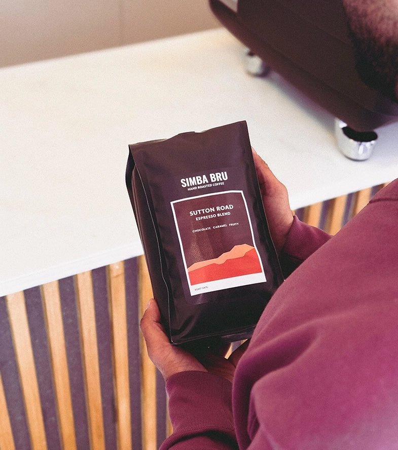 A man holds a coffee bag in front of a counter, showcasing the product