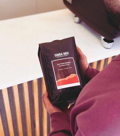 A man holds a coffee bag in front of a counter, showcasing the product
